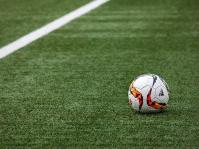 a white and orange soccer ball sits on green astro turf