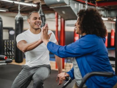 A man and a woman on stationary bikes high five each other